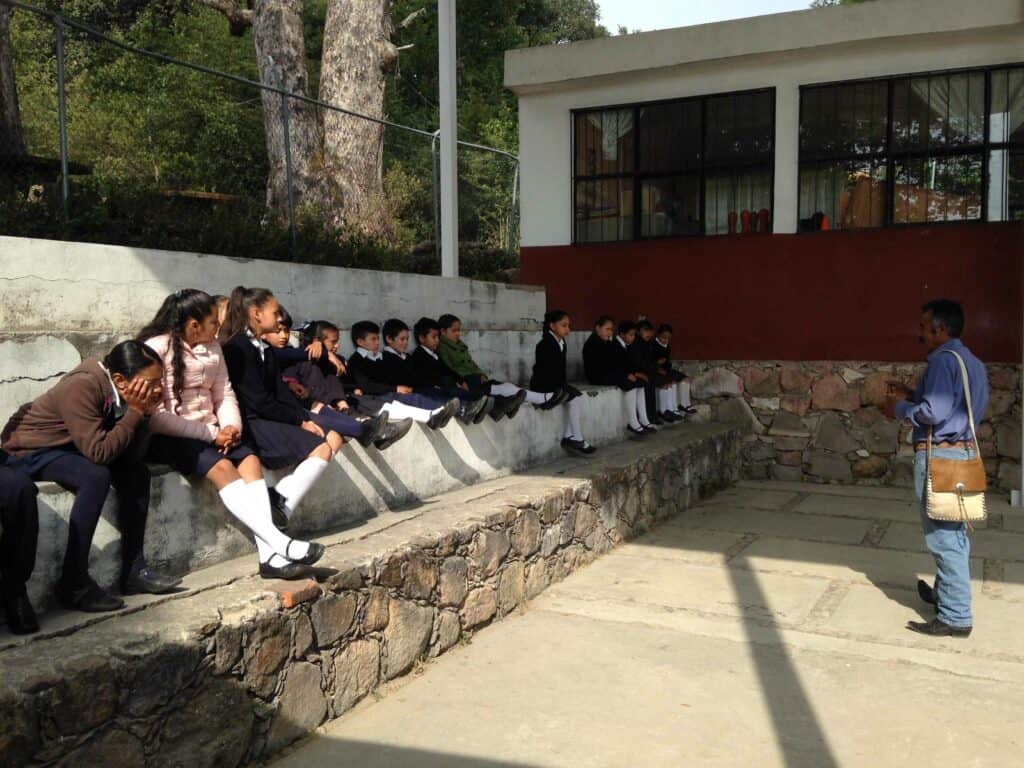 School kids sitting on a wall, listening to their teacher